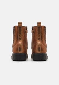 Botas de tobillo de cuero marrón con un acabado texturizado y una suela de goma negra. Las características incluyen una cremallera y acentos decorativos en los laterales.