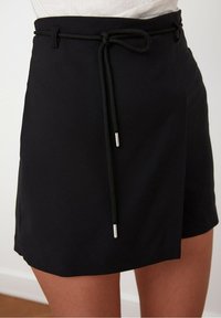 Korte zwarte shorts met een koord in de taille, gemaakt van een soepele stof. Heeft een minimalistisch ontwerp en zilveren hardware accenten aan de uiteinden van het koord.