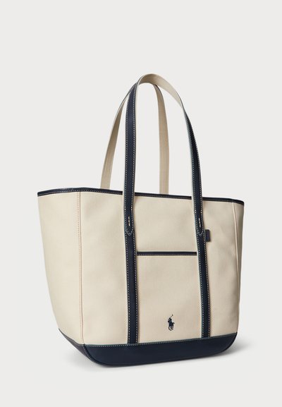 Bežová plátenná taška s námorníckymi modrými akcentmi, dvojitými rúčkami, prednou kapsou a viditeľným prešívaním. Na prednej strane sa nachádza malé logo.