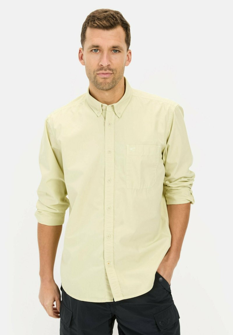 Jasnożółta koszula na guziki z jedną kieszenią, podwiniętymi rękawami i jednolitą fakturą. W połączeniu z ciemnymi spodniami cargo.