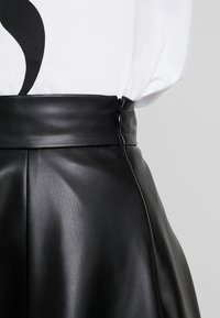 Falda de cuero negra con una cintura alta y cremallera lateral. Presenta una textura suave y pliegues a lo largo de la falda para un detalle de diseño adicional.