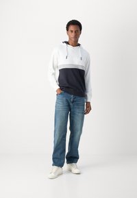 Felpa con cappuccio caratterizzata da blocchi di colore orizzontali bianchi, grigi e blu navy; con cordino e tasca a marsupio; abbinata a jeans azzurri e scarpe da ginnastica bianche.