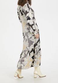 Lång, flödande klänning med ett blommönster i beige och grå nyanser, med långa ärmar och en volangkant. Parat med krämfärgade klackstövlar.