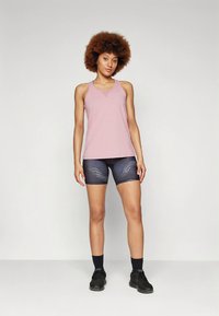 Light pink tank top with a V-neckline paired with patterned navy shorts. Model wears black socks and athletic shoes, standing in a neutral pose.