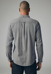 Graues Langarmhemd mit Kentkragen, das ein dezentes strukturiertes Muster, einen Rückenfalte und Knopfakzente an den Manschetten aufweist.