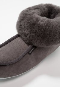 Pantofole in suede grigio con un morbido risvolto in lana grigia, caratterizzate da un design elegante e una fodera interna morbida. Include un'etichetta del marchio sul lato.