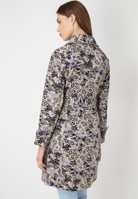Trench coat con estampado floral que presenta una base Beige con diseños en azul marino y azul claro, acentos de botones y detalle de cintura ajustada.