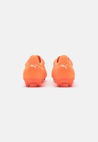 Felroze voetbal schoenen met een gestructureerde bovenkant, een laag profiel ontwerp en paarse gripnoppen op de zool. Puma-logo op elke schoen.