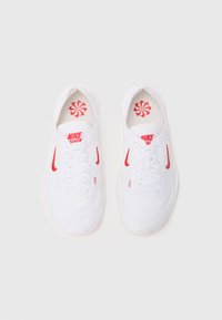 Hvide mesh sportssko med røde accenter, der har et snørebåndsdesign, polstret krave og indersåler med blomstermønster. Nike-logoet er synligt.
