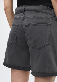 Μαύρο denim σορτς με ψηλή μέση, γυρισμένα τελειώματα και ορατές πίσω τσέπες φορεμένα από ένα άτομο με μαύρο τοπ, εμφανίζονται από πίσω.