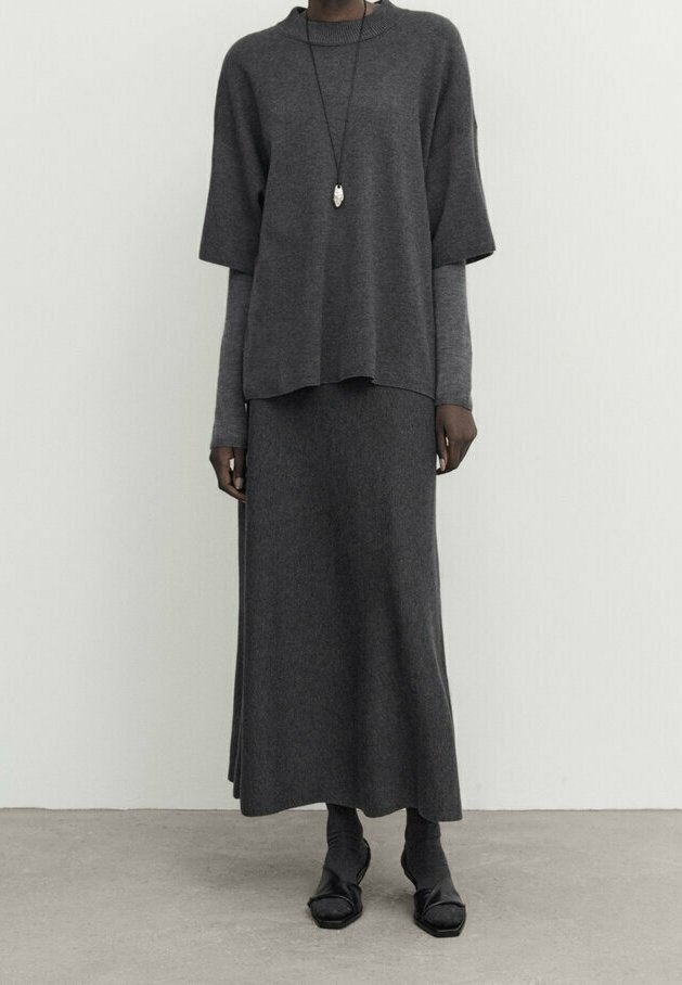 Haut en tricot gris foncé à manches courtes superposé sur une jupe longue assortie. La tenue présente une coupe décontractée et une texture lisse, accompagnée de chaussures noires.