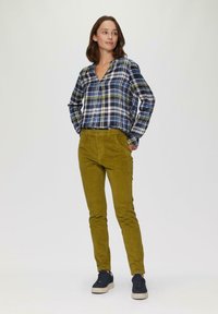 Kariertes Hemd mit Knöpfen in Blau, Grün und Weiß; gelbe Cord-Hosen; marineblaue Sneakers mit weißen Sohlen. Minimalistisches Design, lässige Passform.