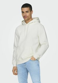Weißer Kapuzenpullover mit Kordelzügen, Fronttasche und gerippten Bündchen, kombiniert mit hellblauen Jeans. Glatte Textur, lässiges Design.