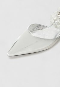 Scarpa argento con punta affusolata e finitura lucida; presenta un accento floreale trasparente sul tacco e un interno metallico.