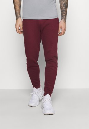 Pantaloni jogger in cotone bordeaux con polsini a costine, abbinati a una t-shirt aderente grigio chiaro e scarpe sportive bianche.