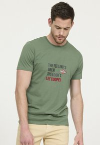 T-shirt en coton vert avec encolure ronde ; présente un texte audacieux en noir, gris et rouge promouvant "Lee Cooper". Manches courtes et coupe régulière.