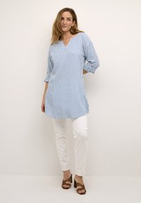 Sinine ja valge triibuline tunika V-kaelusega, kolmeveerandvarrukatega ja külgaukudega, kombineeritud valgete pükstega ja pruunide ploki kontsaga sandaalidega.