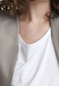 Ljusgrå blazer över en vit t-shirt, som visar en mjuk textur och rund halsringning. Närbild av tyget med synliga sömnadsdetaljer.