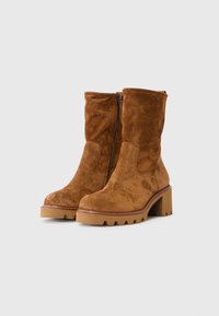 Bottes en suède marron à la cheville avec une fermeture éclair sur le côté, semelle épaisse et finition texturée. Présentent un bout rond et des coutures contrastées le long de la semelle.