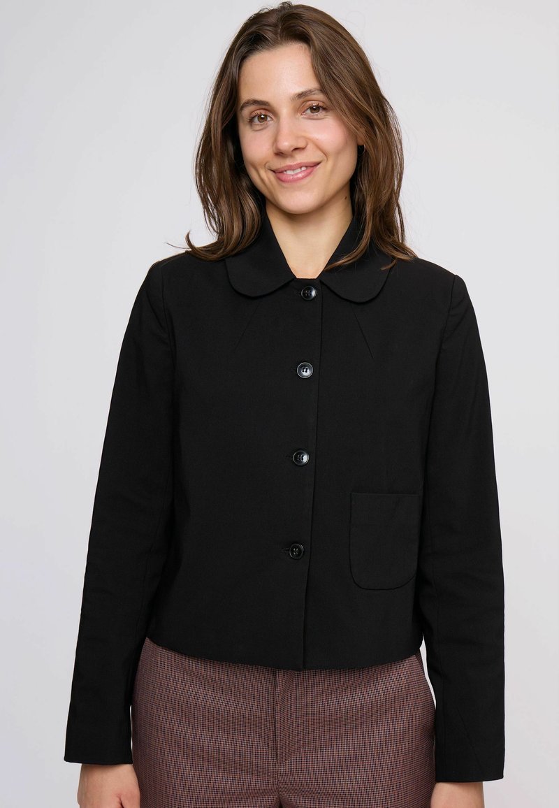 Čierna bunda s zaobleným golierom, ktorá má predné vrecko a zapínanie na gombíky. Tkanina vyzerá hladko a štruktúrovane, doplnená elegantnými gombíkmi.