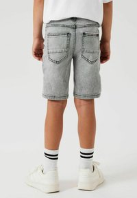Grå denimshorts med rak passform, fransad nederkant och två bakfickor. Bärs med vita sneakers och svartsrandiga strumpor.