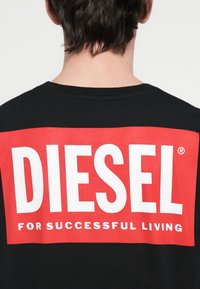 Must t-särk, millel on suur punane ristkülik, mille sees on valgete paksude tähtedega sõna "DIESEL" ja all väiksemate valgete tähtedega tekst "FOR SUCCESSFUL LIVING".