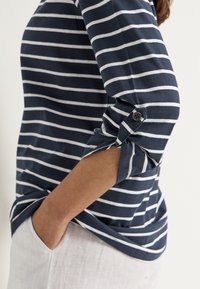 Navy-blau und weiß gestreiftes Hemd mit Dreiviertelärmeln, das über einen Knopfdetail an den aufgerollten Ärmeln und eine lockere Passform verfügt.
