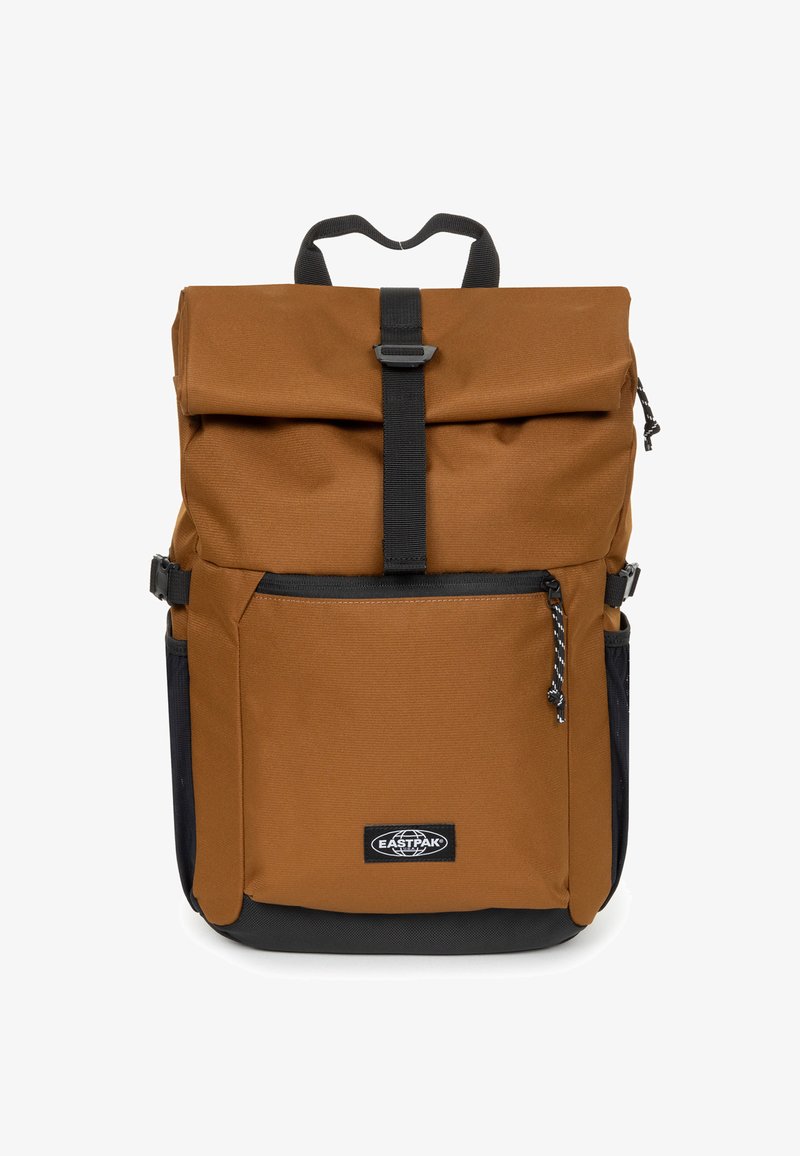 Mochila de tela marrón con cierre enrollable, acentos negros, correas ajustables, bolsillo frontal con cremallera y bolsillos laterales de malla. Logo en el panel frontal.