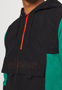 Pullover nero e verde con zip frontale, cappuccio con cordino e grande tasca frontale con logo in rilievo. Dettagli con zip rossa.