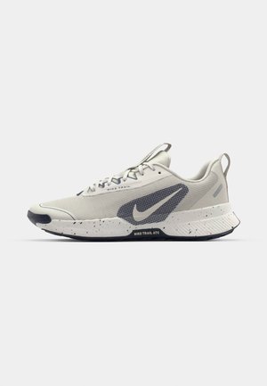 Pantofii de alergare gri deschis, cu un superior sintetic texturat, accente albastre, o talpă intermediară cu pete și un vârf rotunjit. Prezintă în mod proeminent marca Nike.