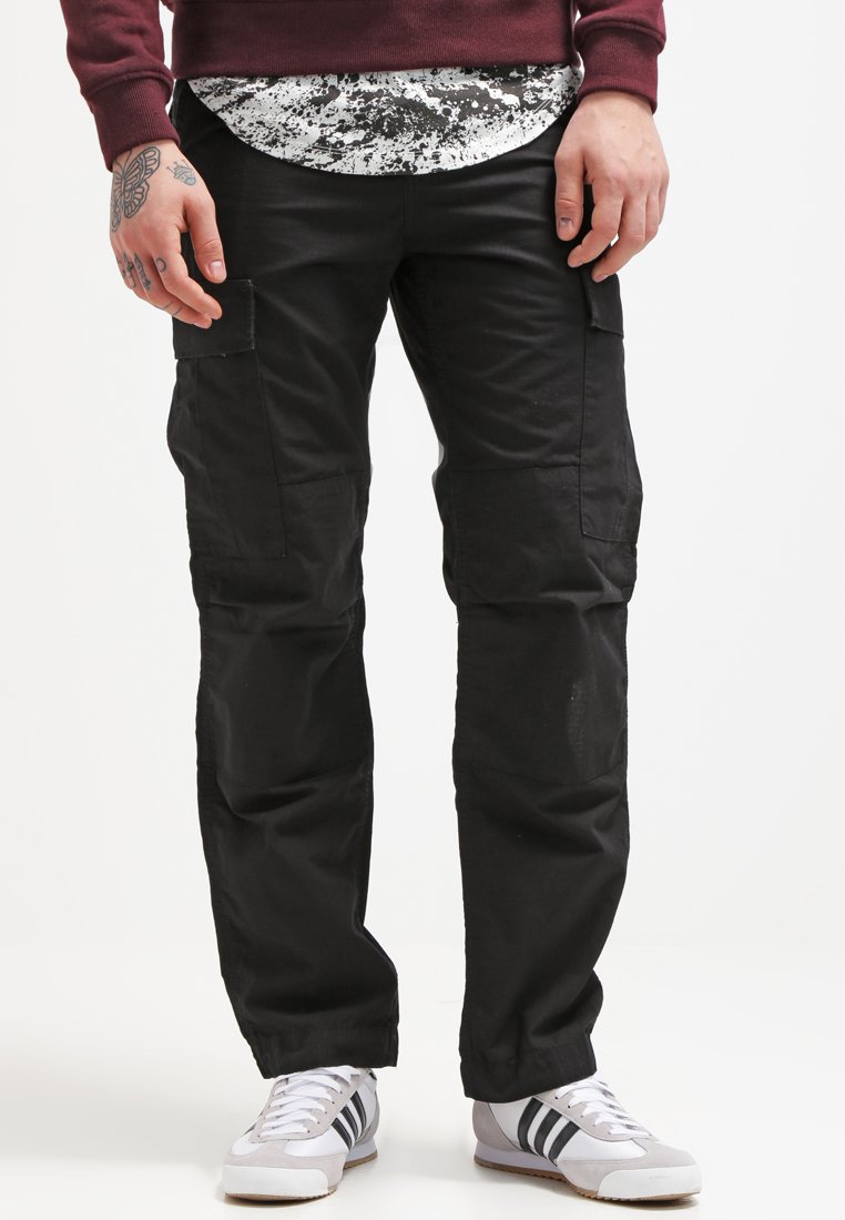 Pantalons cargo noirs avec plusieurs poches, fabriqués à partir d'un tissu résistant. Associés à des baskets blanches avec des bandes noires et une chemise imprimée en dessous.