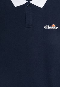 Polo shirt blu navy in cotone, con colletto bianco, patta con due bottoni e un piccolo logo bianco con accento arancione e bianco.