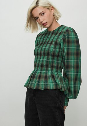 Blusa verde a quadri con maniche lunghe a sbuffo, vita arricciata e orlo a peplum. Il tessuto ha un aspetto testurizzato con accenti scuri.
