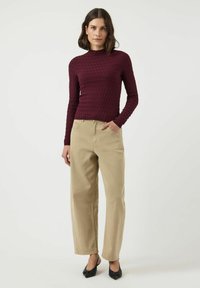 Bordowy prążkowany top z długim rękawem i wysokim kołnierzem, w połączeniu z beżowymi spodniami o szerokich nogawkach i czarnymi szpilkami w szpic. Prosty, teksturowany design.