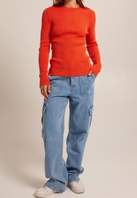 Haut à manches longues rouge à côtes associé à un jean cargo bleu ample et des baskets blanches. Le jean dispose de poches latérales et d'une coupe décontractée.