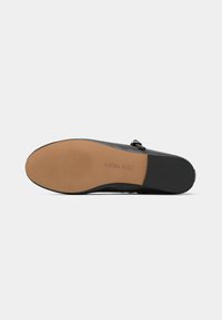 Zapato de cuero negro con una superficie texturizada, suela en capas con un fondo marrón y un detalle de hebilla de metal.