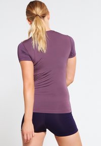 Camiseta deportiva de manga corta en color malva con un diseño ajustado, combinada con pantalones cortos azul marino oscuro. El material parece suave y elástico.