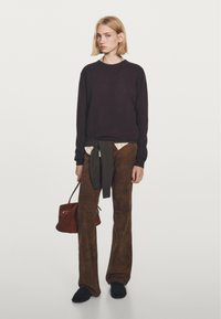 Maglione viola scuro, camicia a colletto crema sotto, pantaloni a palazzo in suede marrone, cintura in tessuto verde, piccola borsa a mano marrone scuro, scarpe nere.