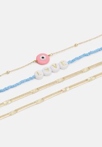 Quatro pulseiras: uma corrente dourada com um charm de olho rosa e preto, uma pulseira de contas azuis com contas brancas em forma de "LOVE", e duas alianças texturizadas em ouro.