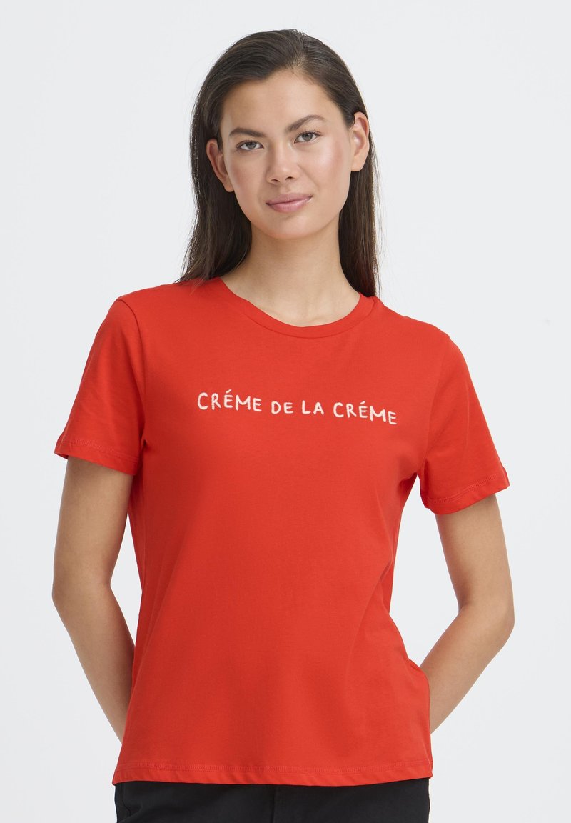 Crvena pamučna majica s natpisom "CRÉME DE LA CRÉME" u kontrastnoj boji, okrugli izrez i kratki rukavi. Glatka tekstura.