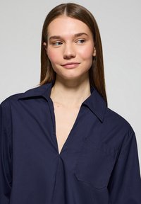 Camicia col colletto blu navy in tessuto liscio, con una mezza apertura e una tasca a toppa singola sul lato sinistro del petto.
