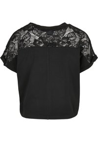 Black top with a lace overlay at the back, loose fit, short sleeves, soft texture, and a rounded hem. Detailed floral lace pattern.