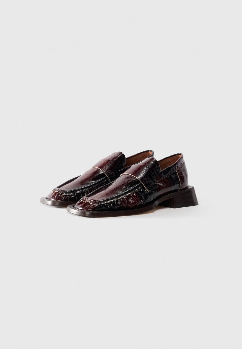 Une paire de mocassins en cuir laqué bordeaux foncé avec un petit talon carré, présentée sur fond blanc.