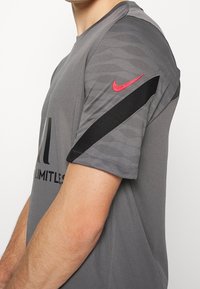 Grå idrottströja i slät tyg, med en svart rand på ärmen och en röd Nike-logotyp. Texten "LIMITLESS" på framsidan.