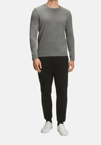 Grå stickad tröja med rund halsringning, med långa ärmar och ribbade muddar, i kombination med svarta slim-fit byxor och vita sneakers.