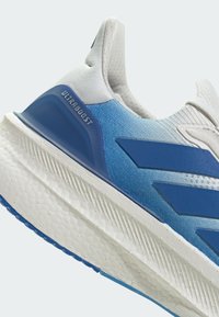 Bijela i plava tenisica za trčanje s gradijentnim dizajnom, teksturiranim gornjim dijelom i istaknutim natpisom "ULTRABOOST" na peti.