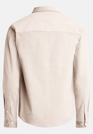 Camisa de manga larga en tejido texturizado beige, con cuello, puños abotonados y un dobladillo curvado con un yugo central en la parte posterior.
