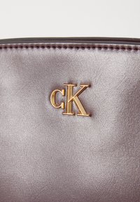 Calvin Klein handtas in glad metallic grijs leer met een gouden "CK" logo. De textuur is zacht met zichtbare stiksels.