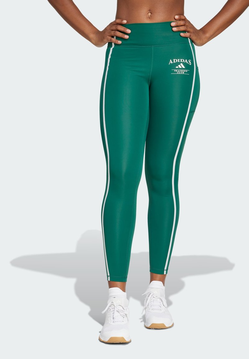 Leggings verdi realizzati in tessuto elasticizzato, con strisce laterali bianche e un logo Adidas sulla parte anteriore. Abbinati a sneaker bianche.