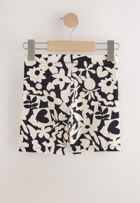 Pantaloni scurți din bumbac cu un model floral negru și crem, având o textură netedă, talie elastică și croială dreaptă, agățați pe o clemă de lemn.